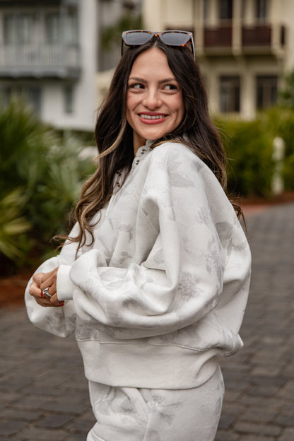 Woman wearing a white sweatshirt and pants with sunglasses on her head, standing outdoors.