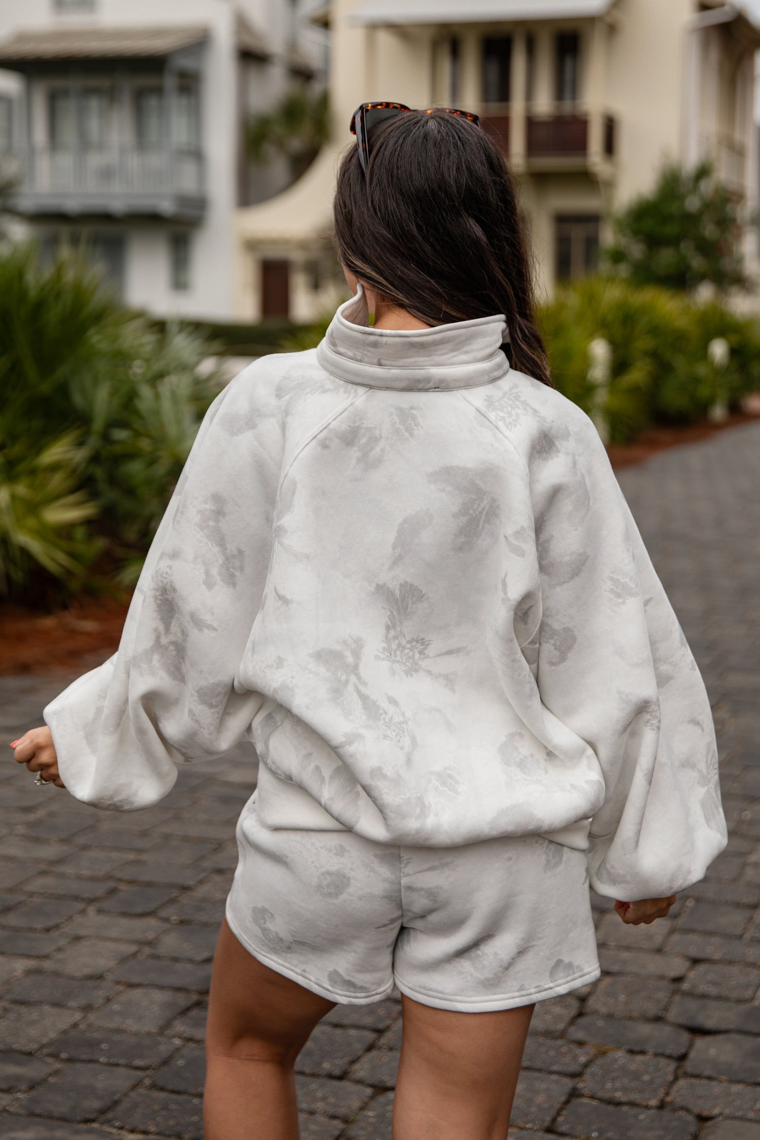 Person wearing a gray tie-dye outfit walking on a street.