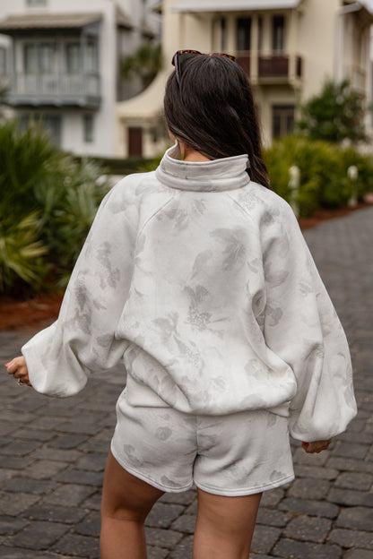 Person wearing a gray tie-dye outfit walking on a street.