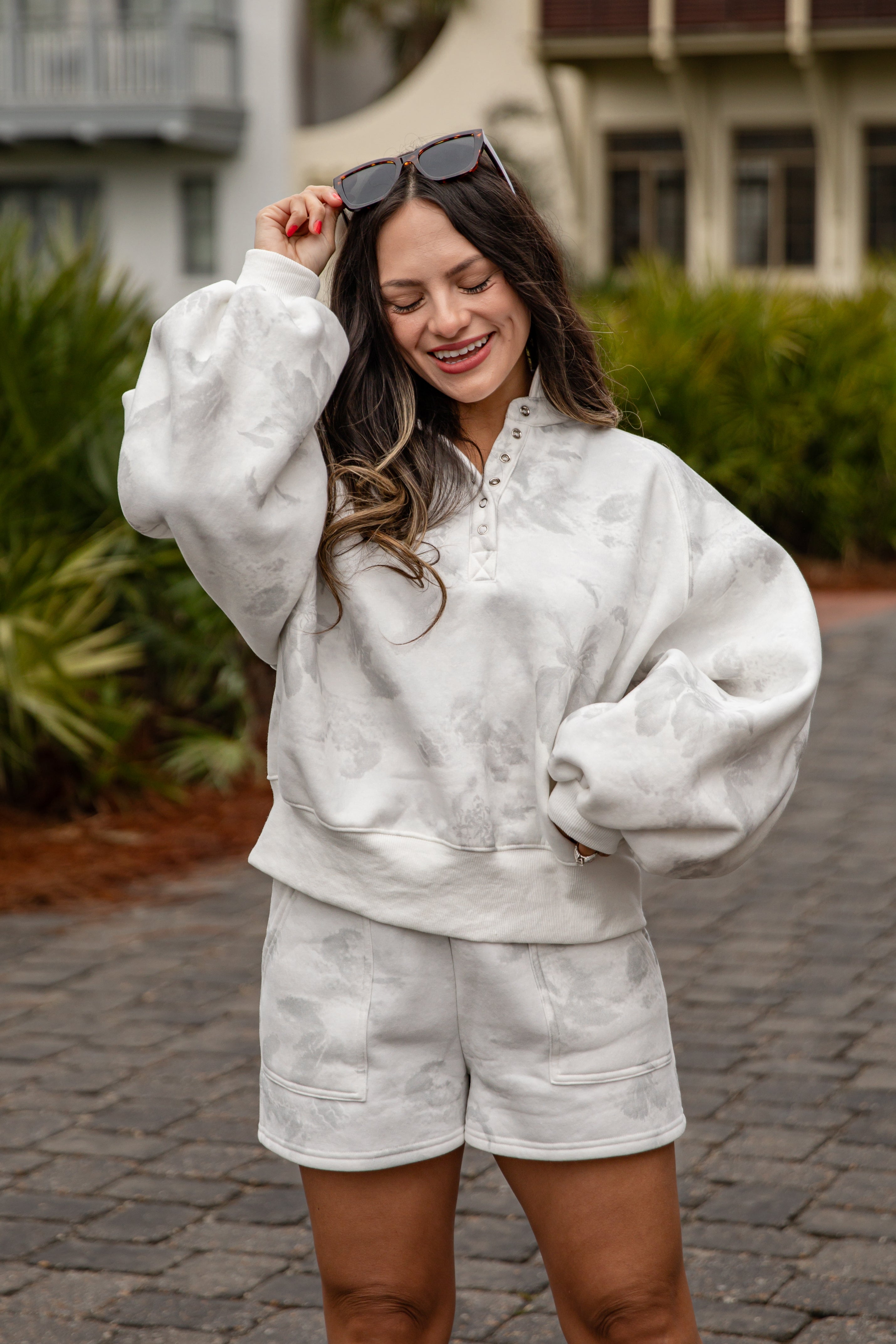 Woman wearing a white tie-dye outfit with sunglasses on a paved path.