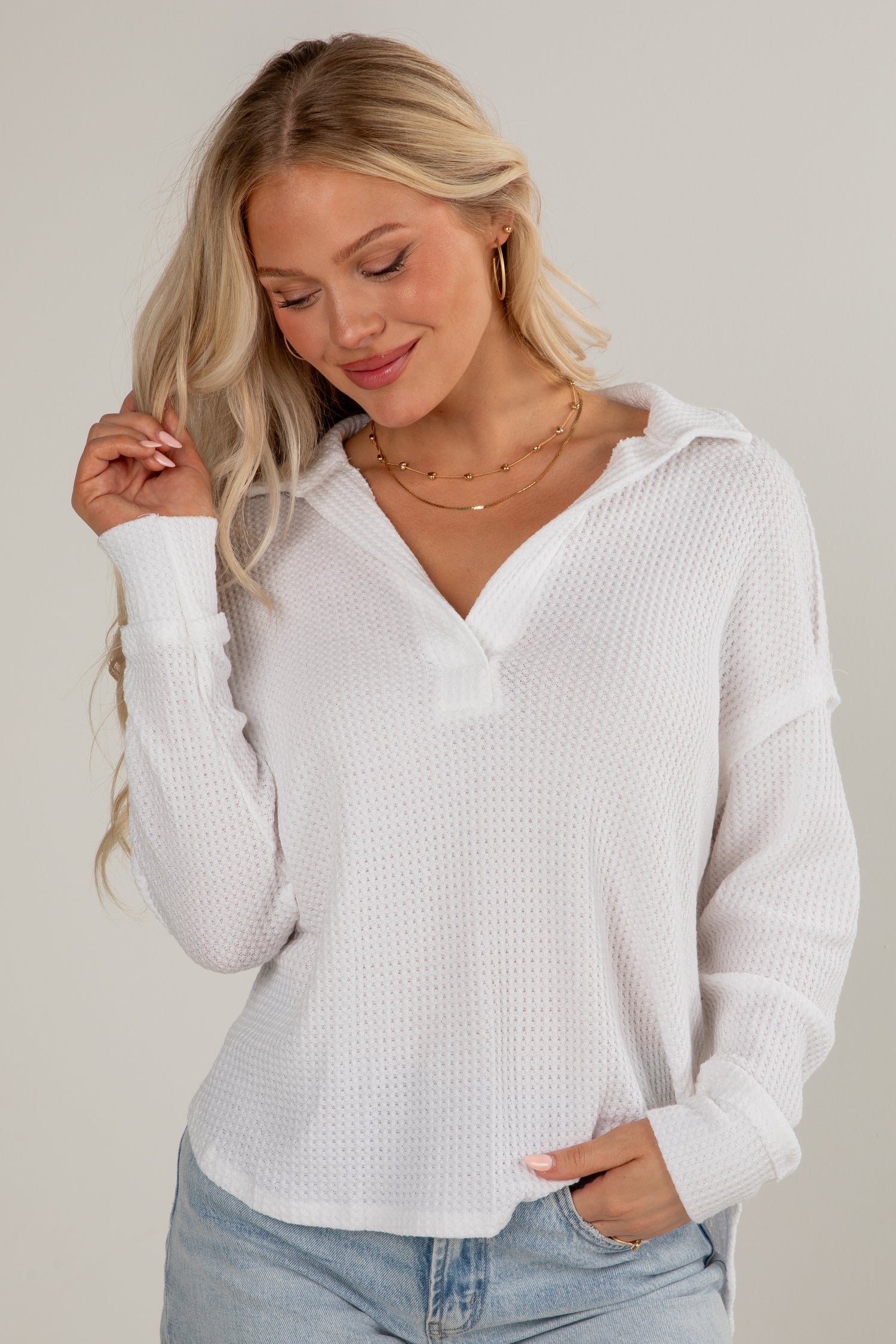 Woman wearing a white long-sleeve top and light blue jeans against a plain background