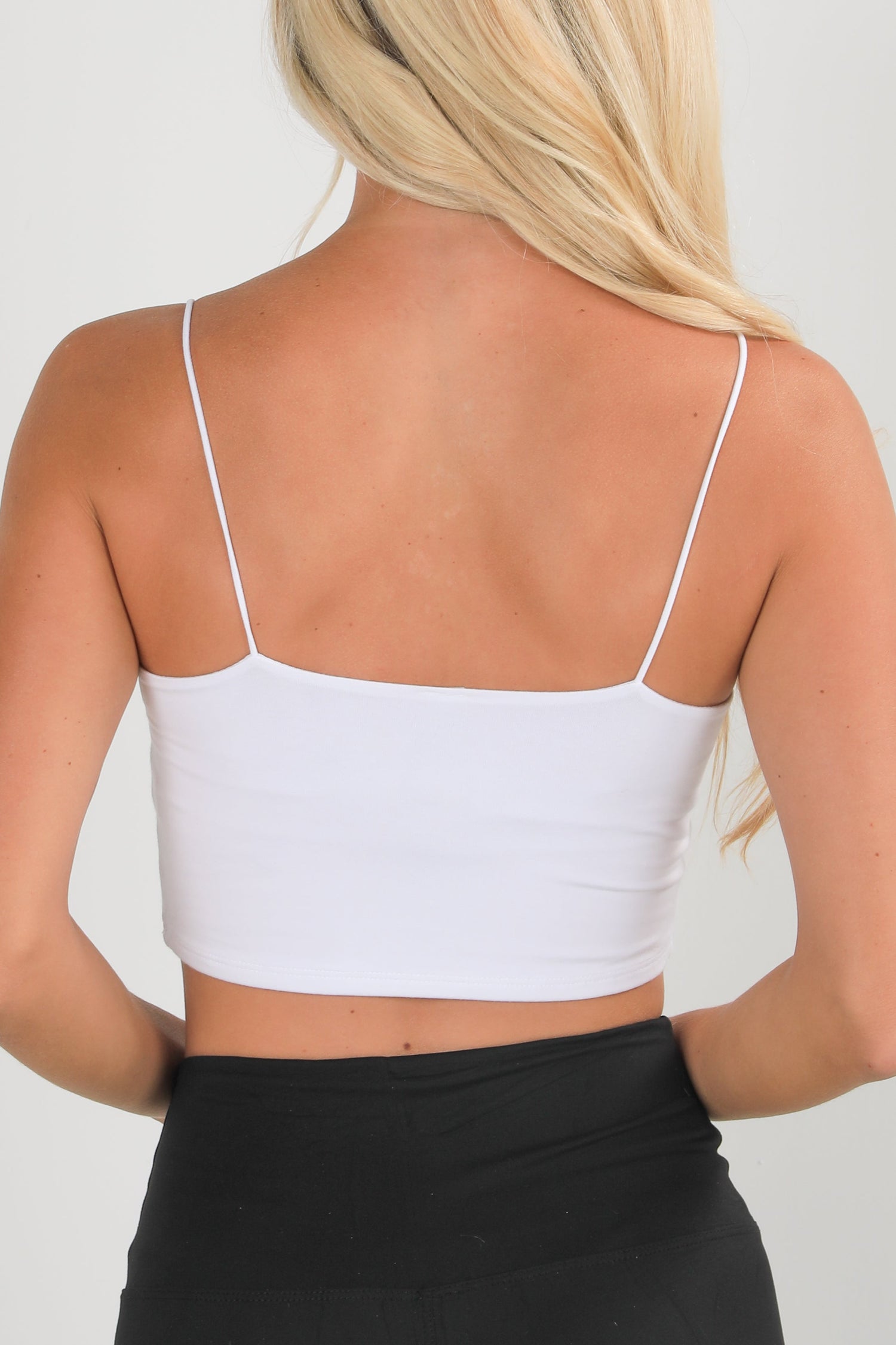 Person wearing a white crop top with thin straps on a plain background