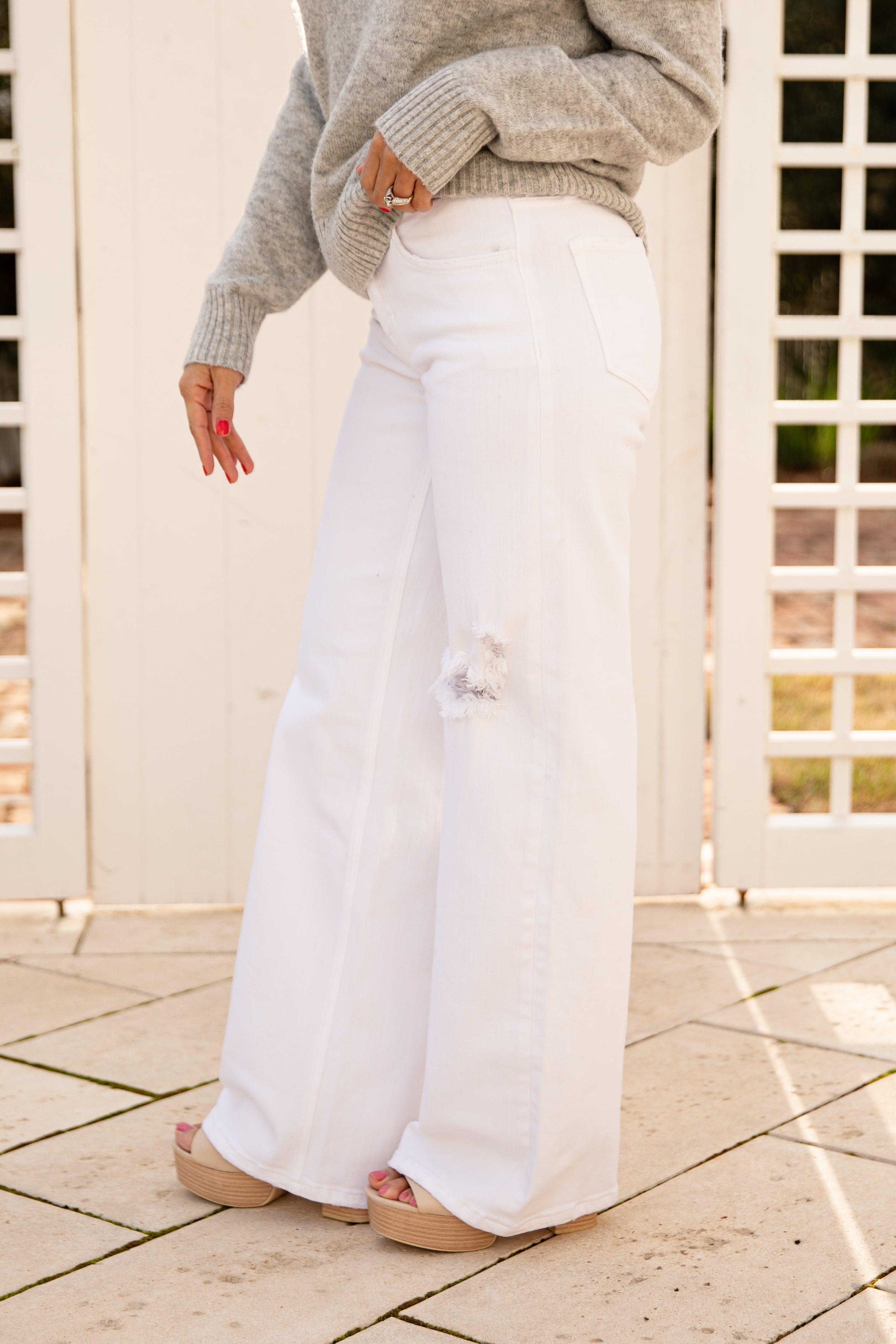 Person wearing a gray sweater and white pants standing on a tiled floor.