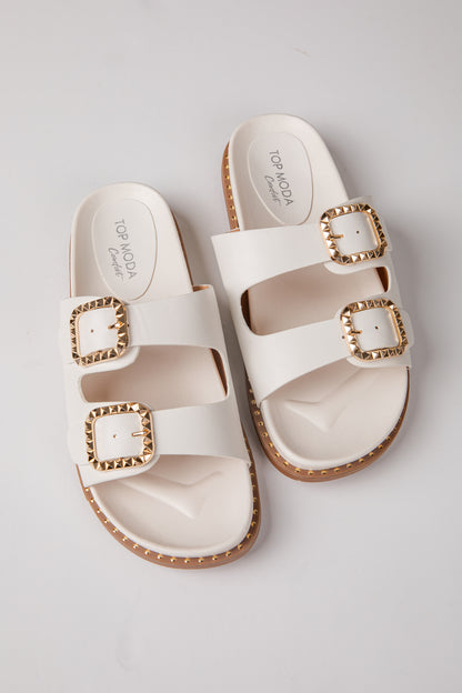 Pair of white sandals with gold buckles on a light gray background