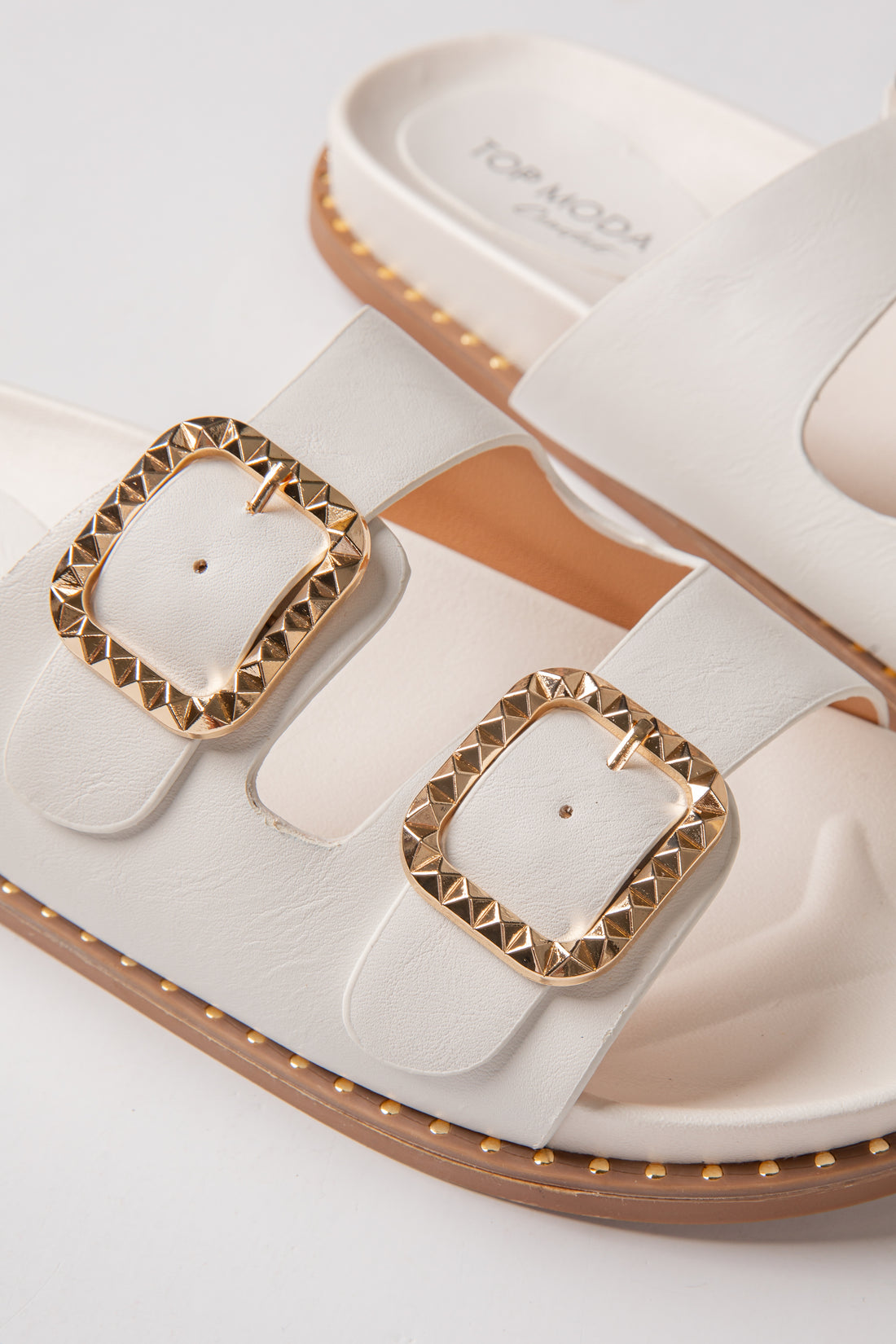 White sandals with gold buckles on a light gray background