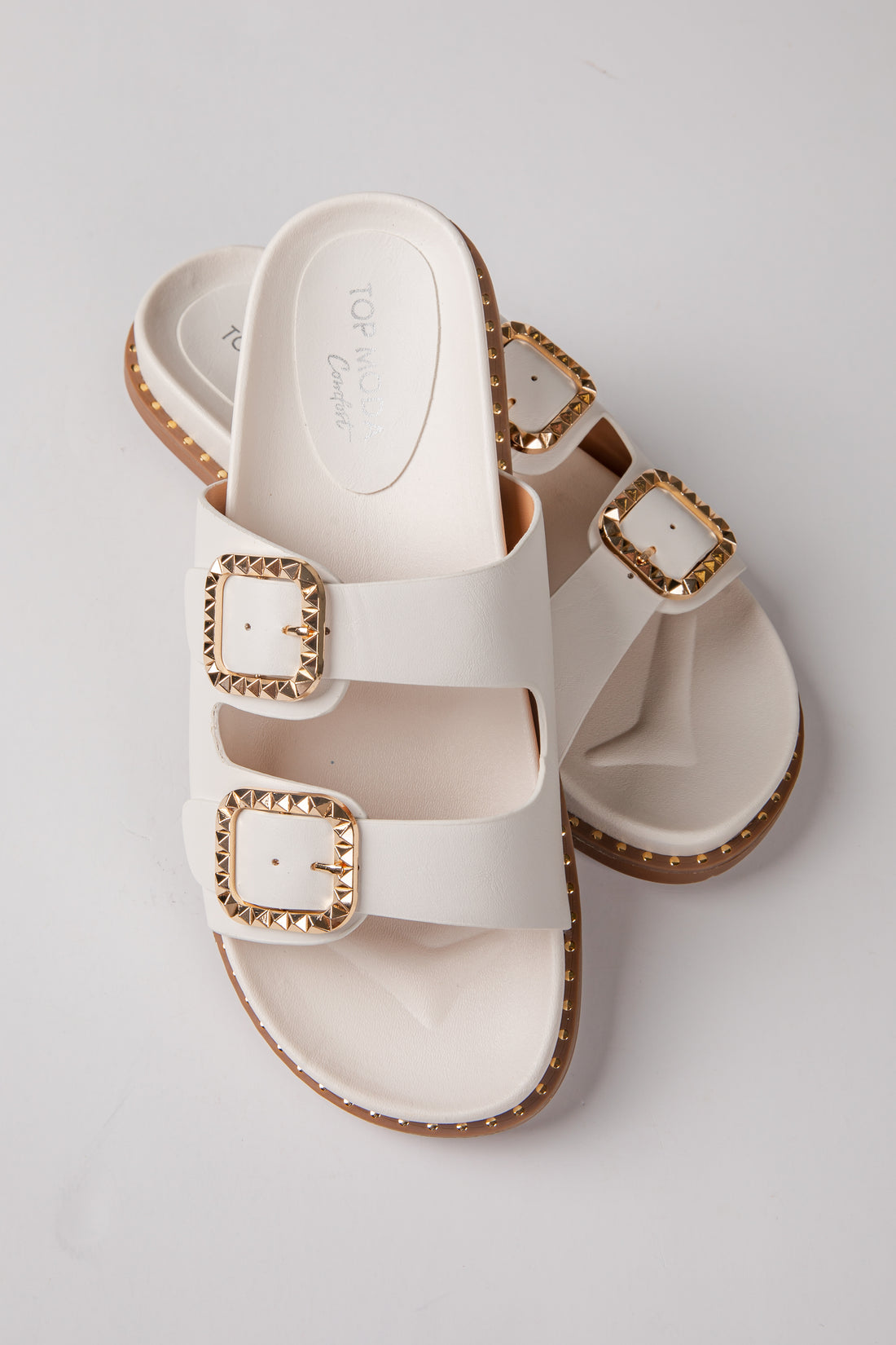 White sandals with gold buckles on a light gray background