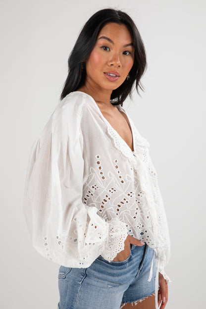Woman wearing a white lace blouse with blue jeans on a plain background