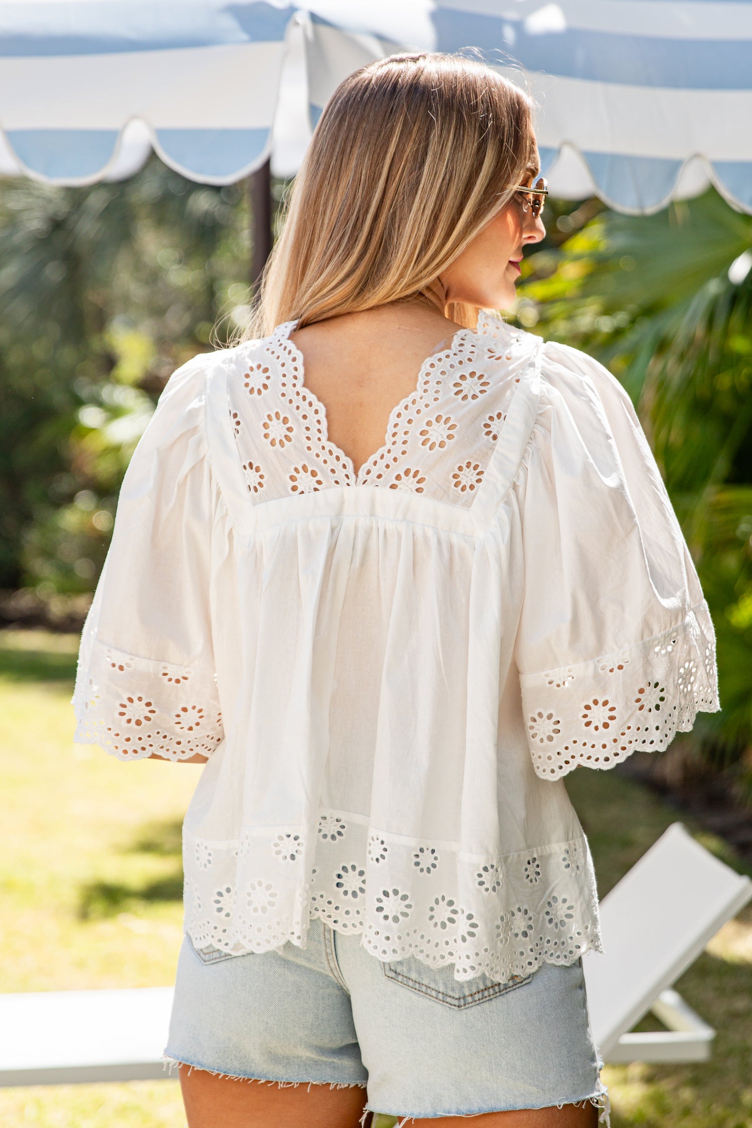 Woman wearing a white blouse with floral lace details in an outdoor setting.