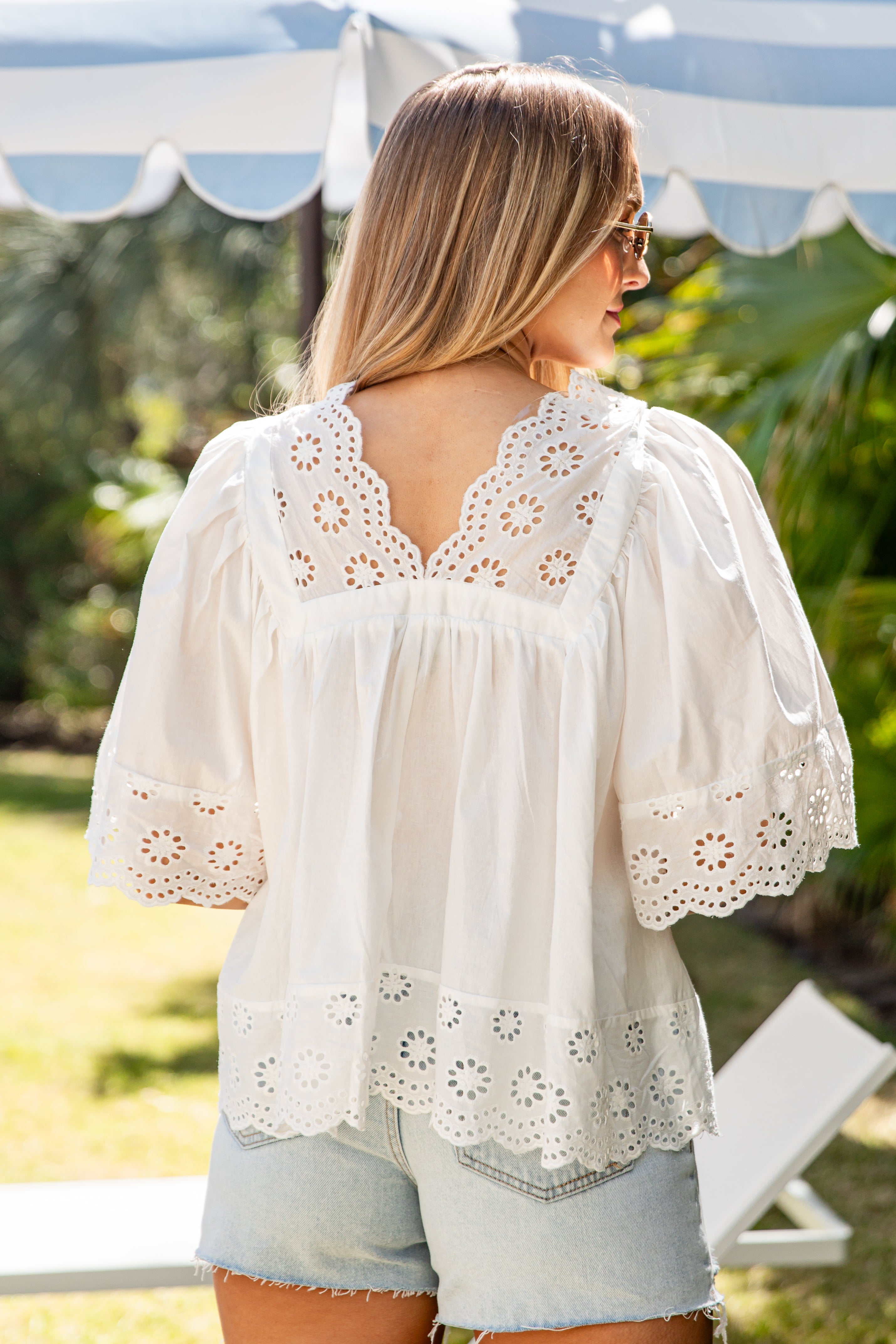 Woman wearing a white blouse with floral lace details in an outdoor setting.