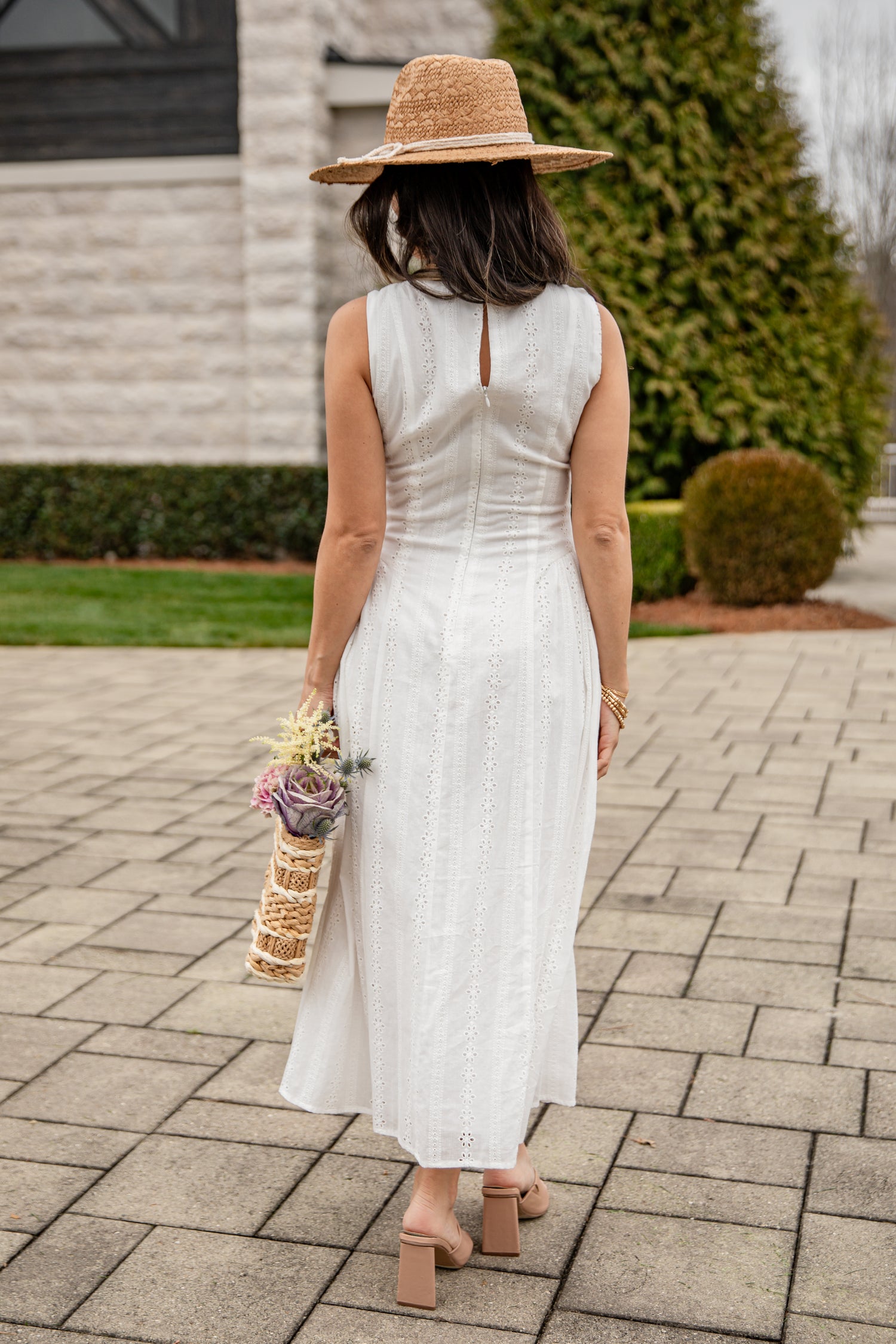 Woman in a white dress and straw hat walking on a paved path.