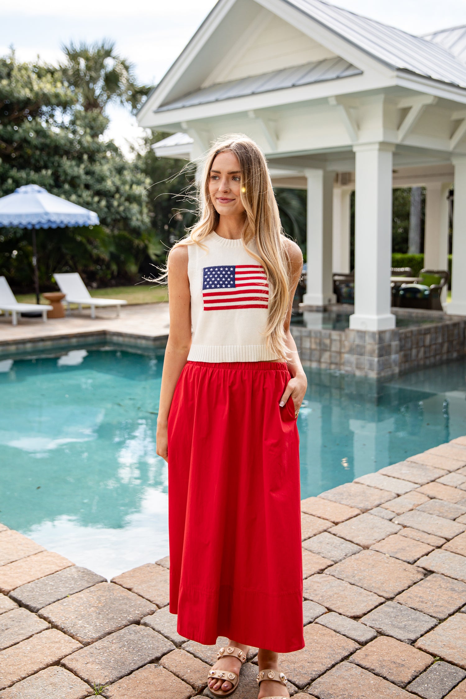 Woman wearing a sleeveless top with an American flag design and a red skirt by a pool.