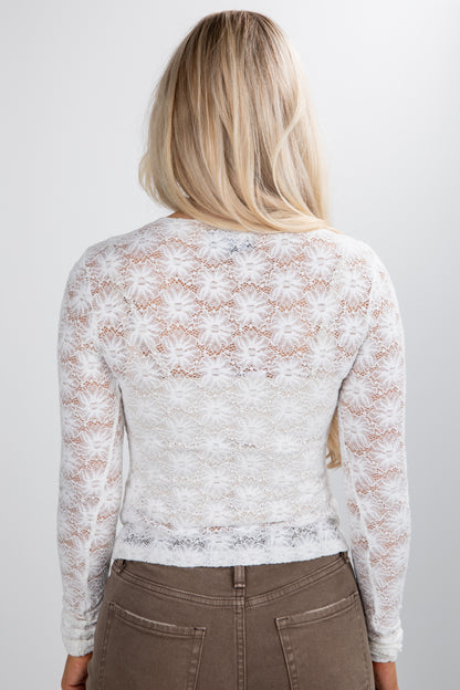 Person wearing a white lace long-sleeve top against a plain background