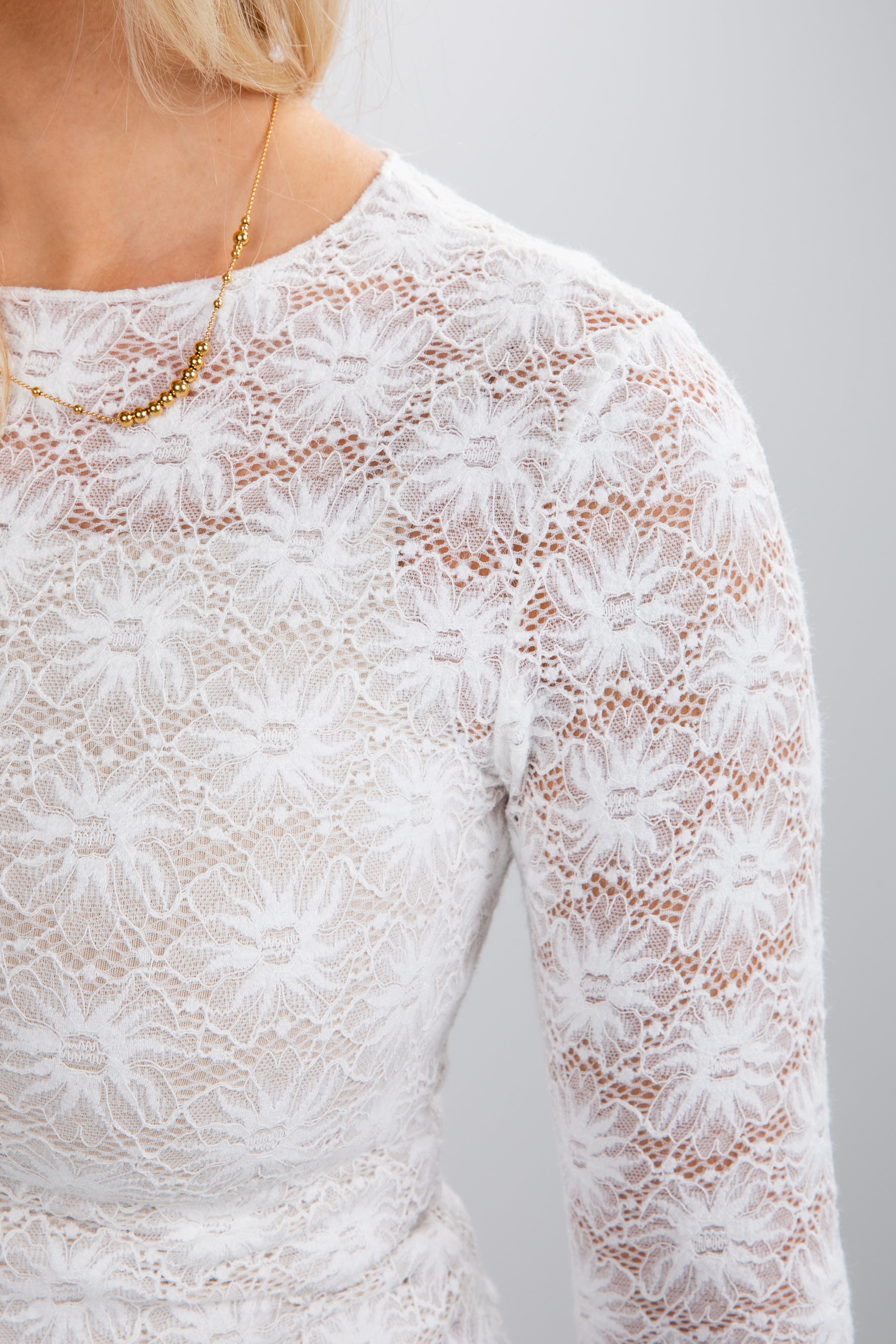 Close-up of a white lace dress with long sleeves on a plain background