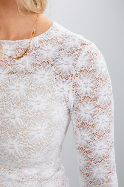 Close-up of a white lace dress with long sleeves on a plain background