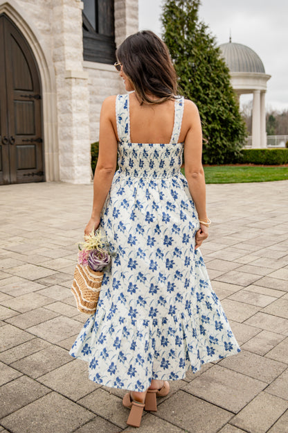 Woman in a floral dress walking outdoors near a building with a dome.