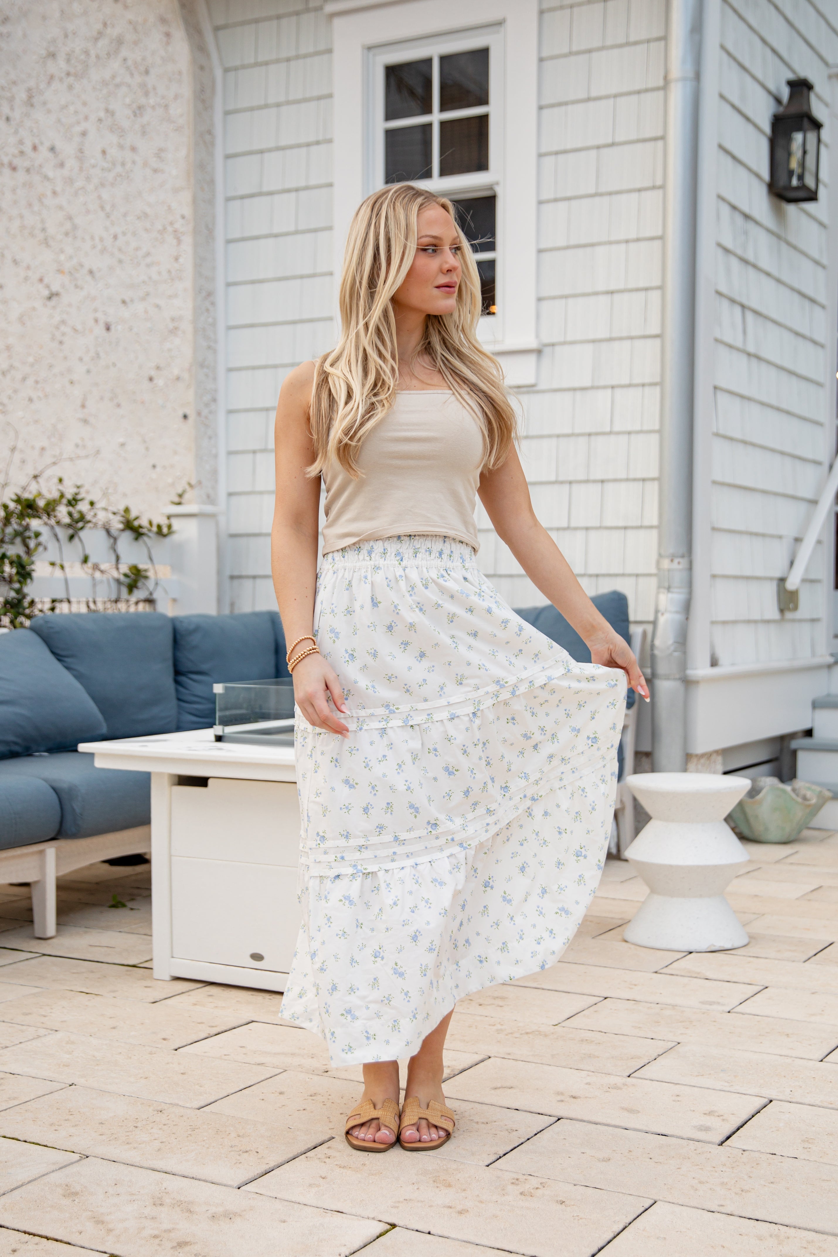 Woman in a beige top and white patterned skirt standing on a patio.