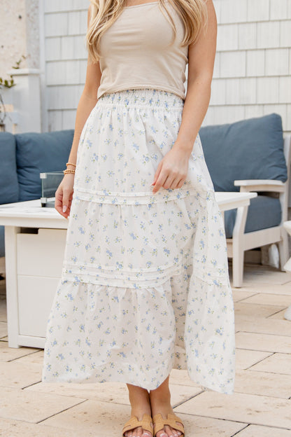 Woman wearing a long floral skirt and beige top in an outdoor setting.