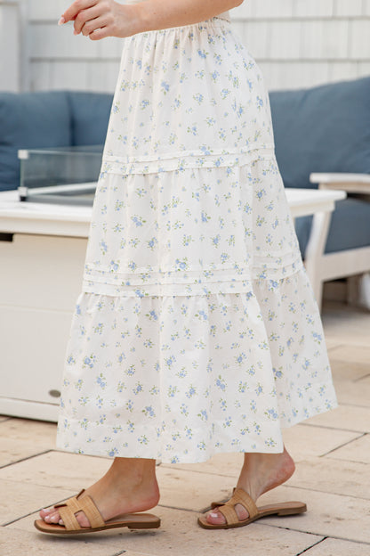 Person wearing a white floral dress standing on a wooden deck.