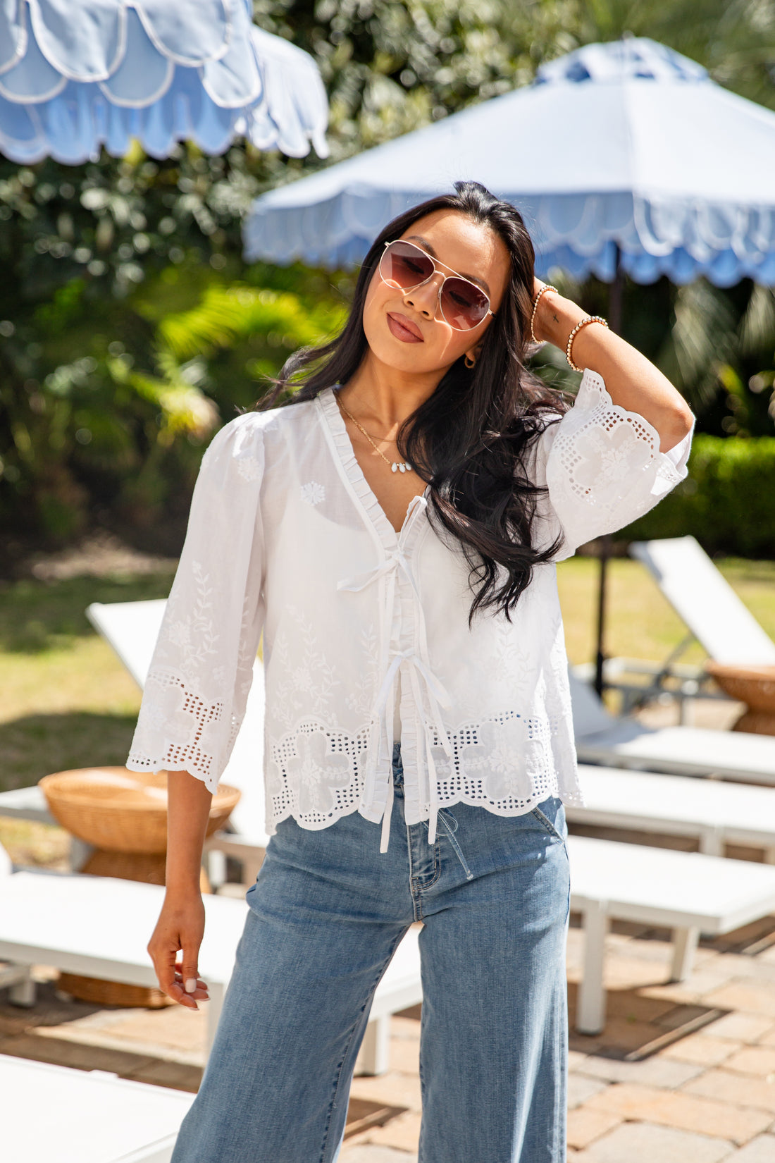 Woman wearing a white lace top and blue jeans in a poolside setting