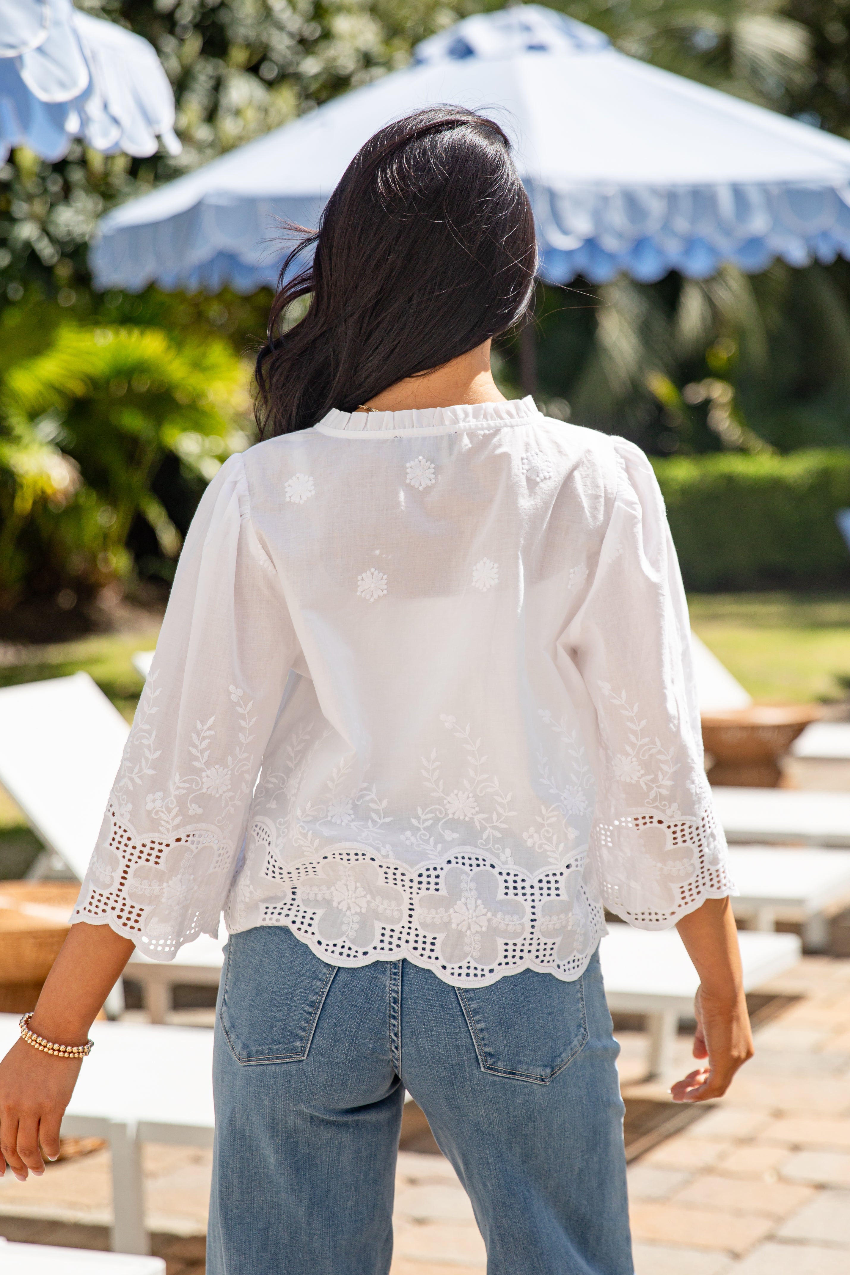 Person wearing a white lace top and blue jeans in an outdoor setting with umbrellas.