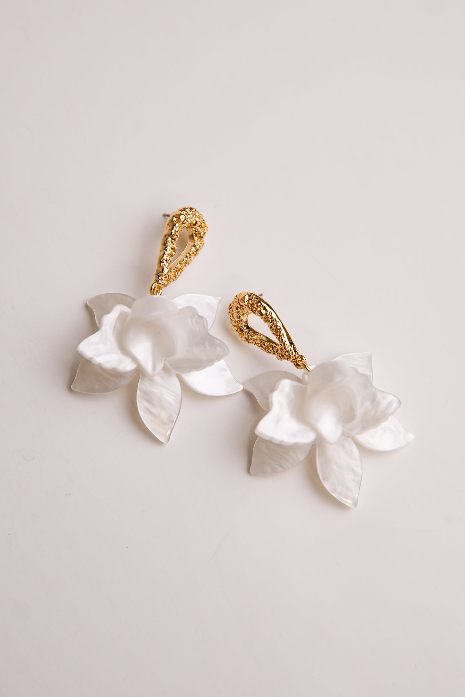 Pair of earrings with white floral designs and gold accents on a light gray background