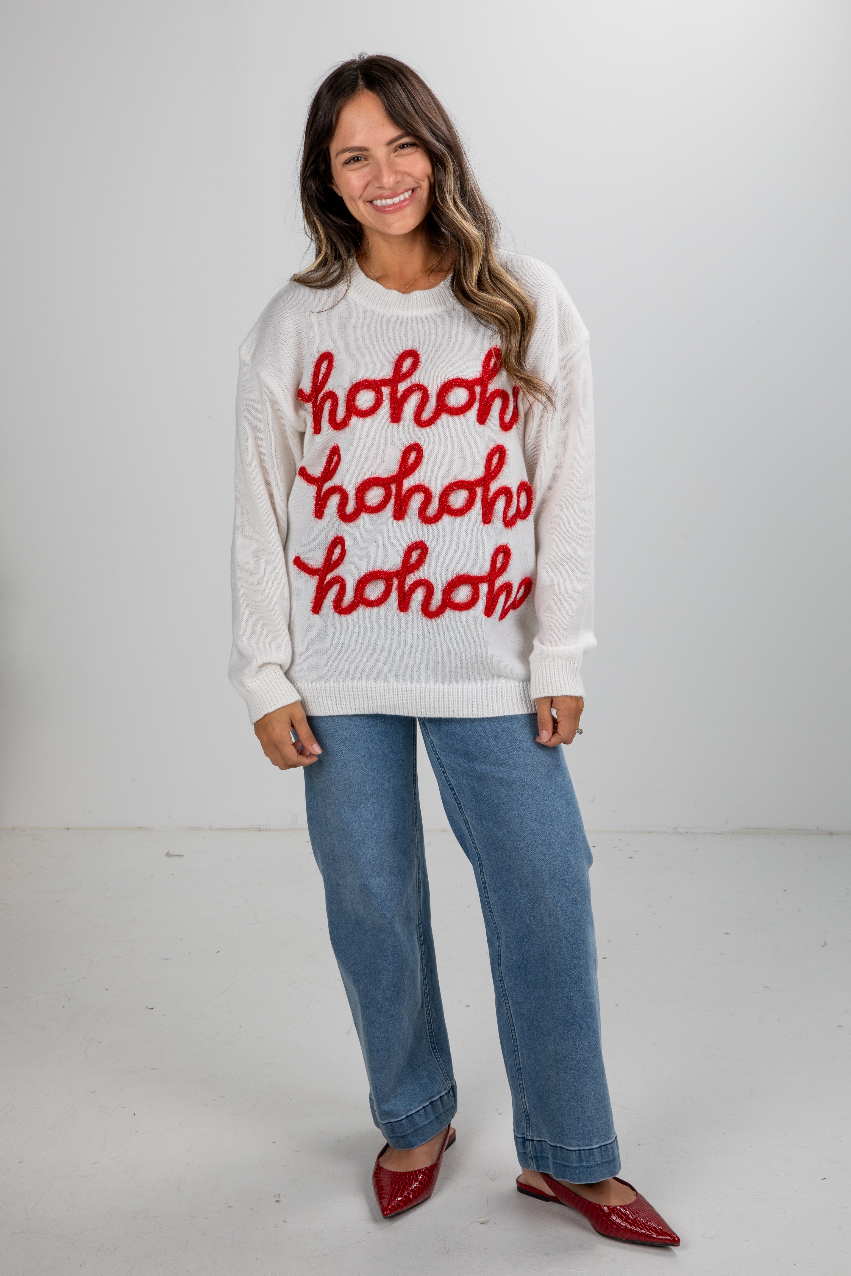 Woman wearing a white sweater with red text and blue jeans on a white background
