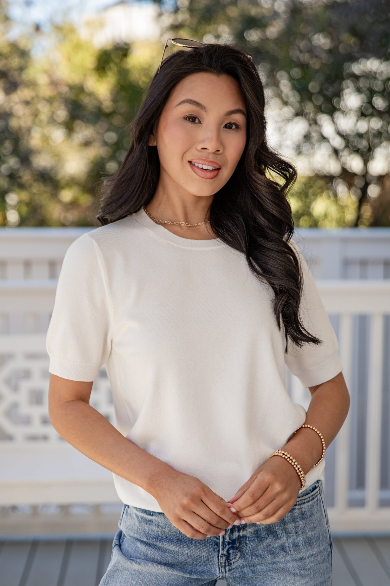 Woman wearing a white t-shirt and blue jeans on a deck with trees in the background