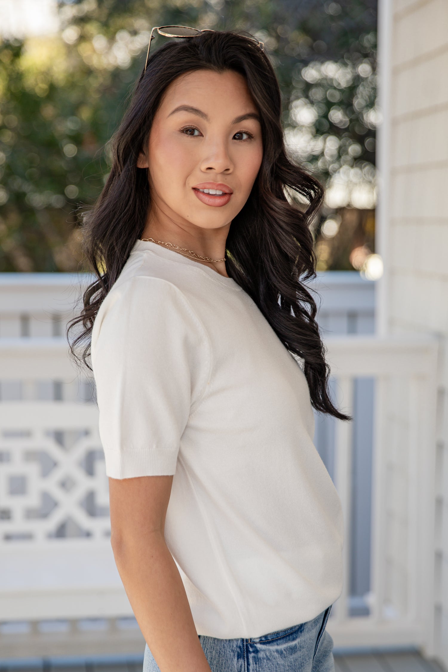 Woman wearing a white t-shirt and blue jeans standing on a porch.