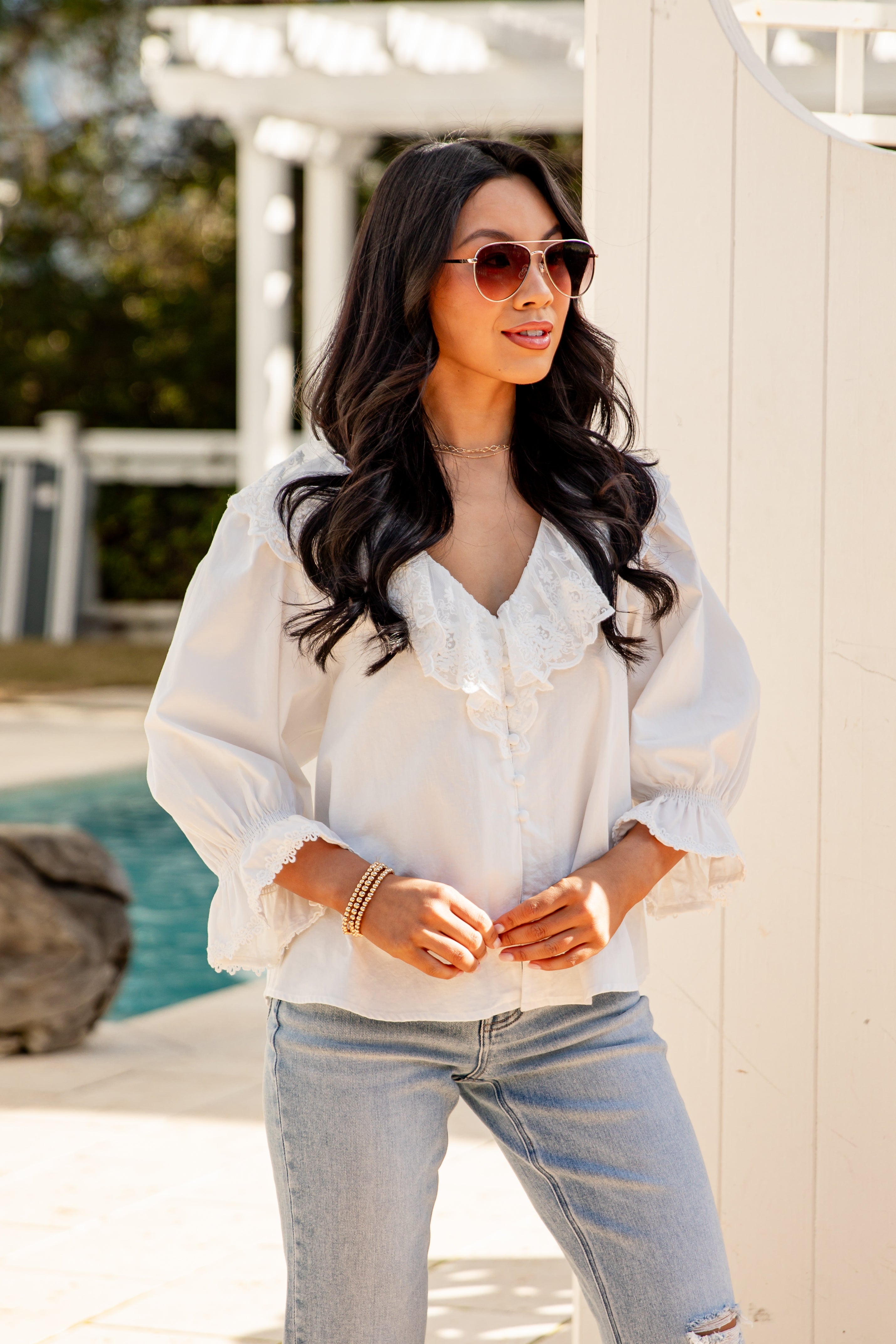 Woman wearing a white blouse and light blue jeans by a poolside.