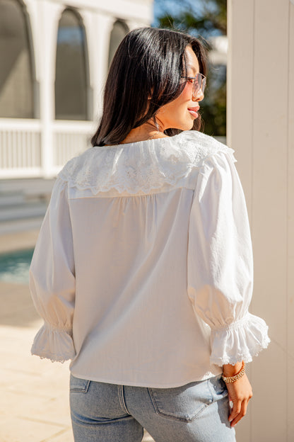 Woman wearing a white blouse with ruffled sleeves in an outdoor setting
