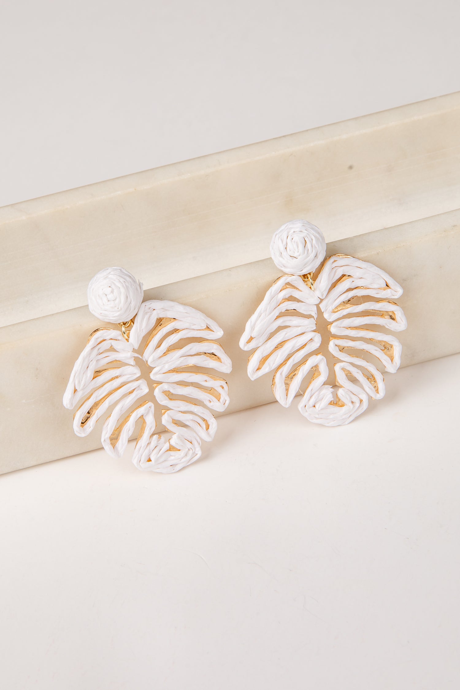 White earrings with gold accents on a light wooden surface