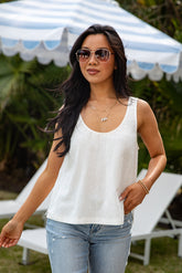 Woman wearing a white tank top and sunglasses outdoors under a striped canopy.