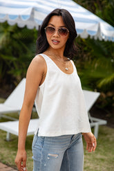 Woman wearing a white sleeveless top and blue jeans outdoors with greenery in the background