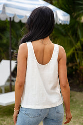 Woman wearing a white sleeveless top and blue jeans with a blurred outdoor background