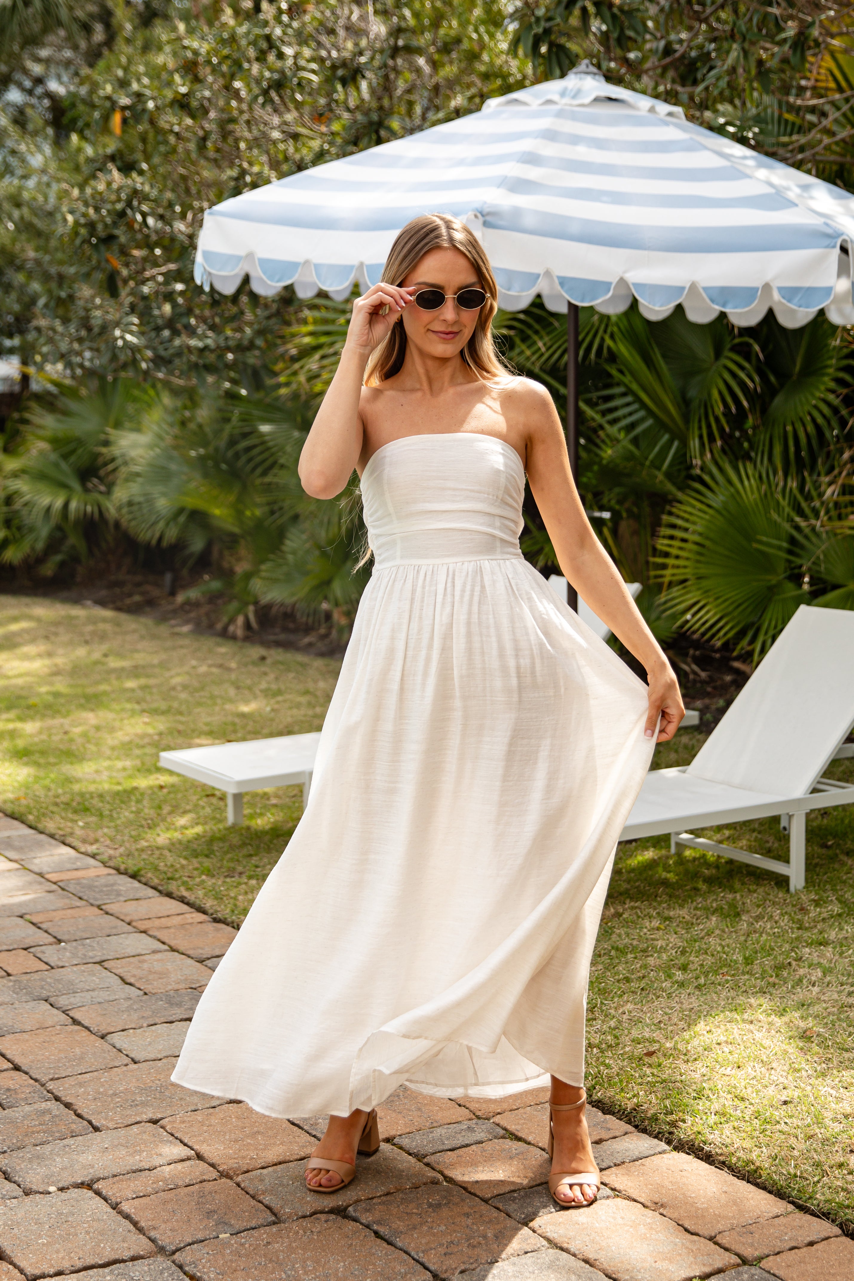 Woman in a white dress standing under a striped umbrella in a garden setting