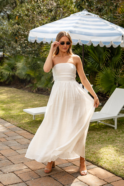 Woman in a white dress standing under a striped umbrella in a garden setting