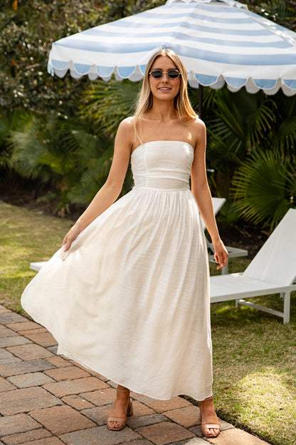 Woman in a white dress standing under a striped umbrella in a garden setting