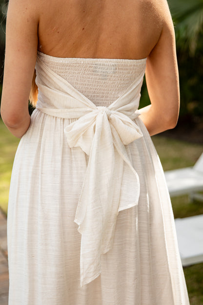 Beige strapless dress with a bow detail on a blurred natural background