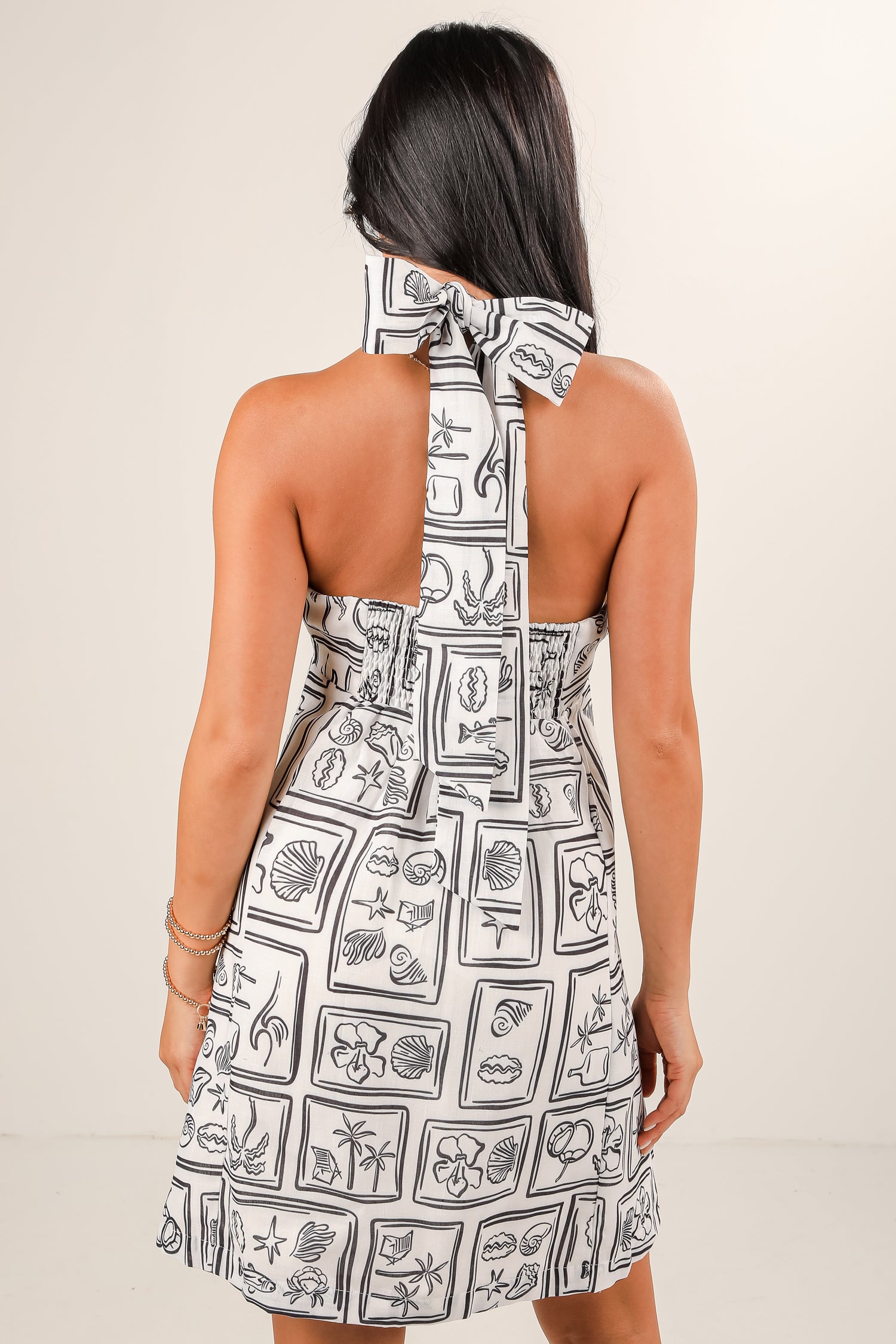 Woman wearing a black and white patterned dress with a bow detail on a beige background