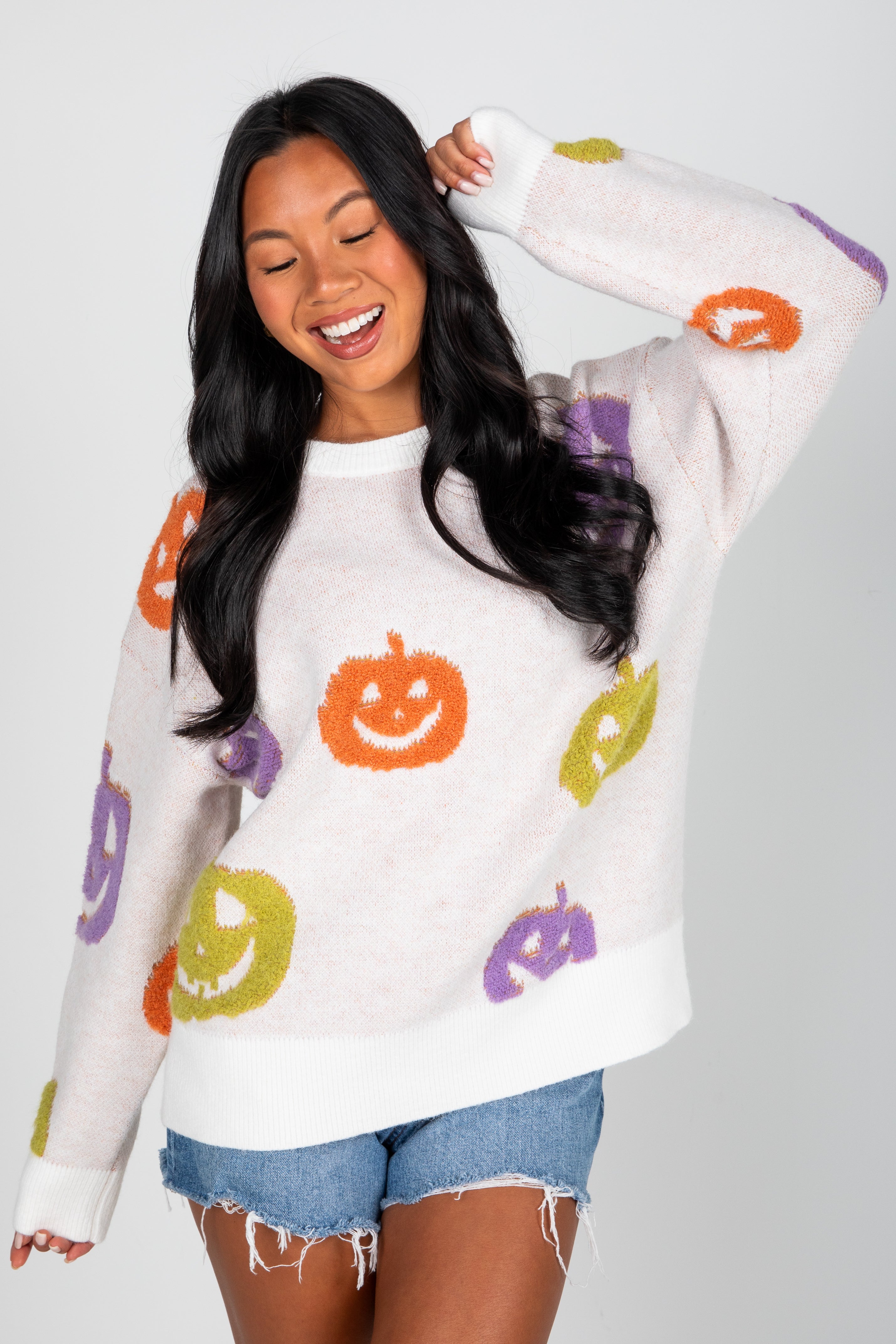 Woman wearing a white sweater with colorful pumpkin patterns on a plain background