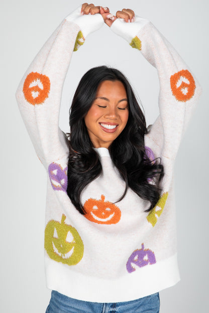 Woman wearing a white hoodie with colorful pumpkin designs on a gray background