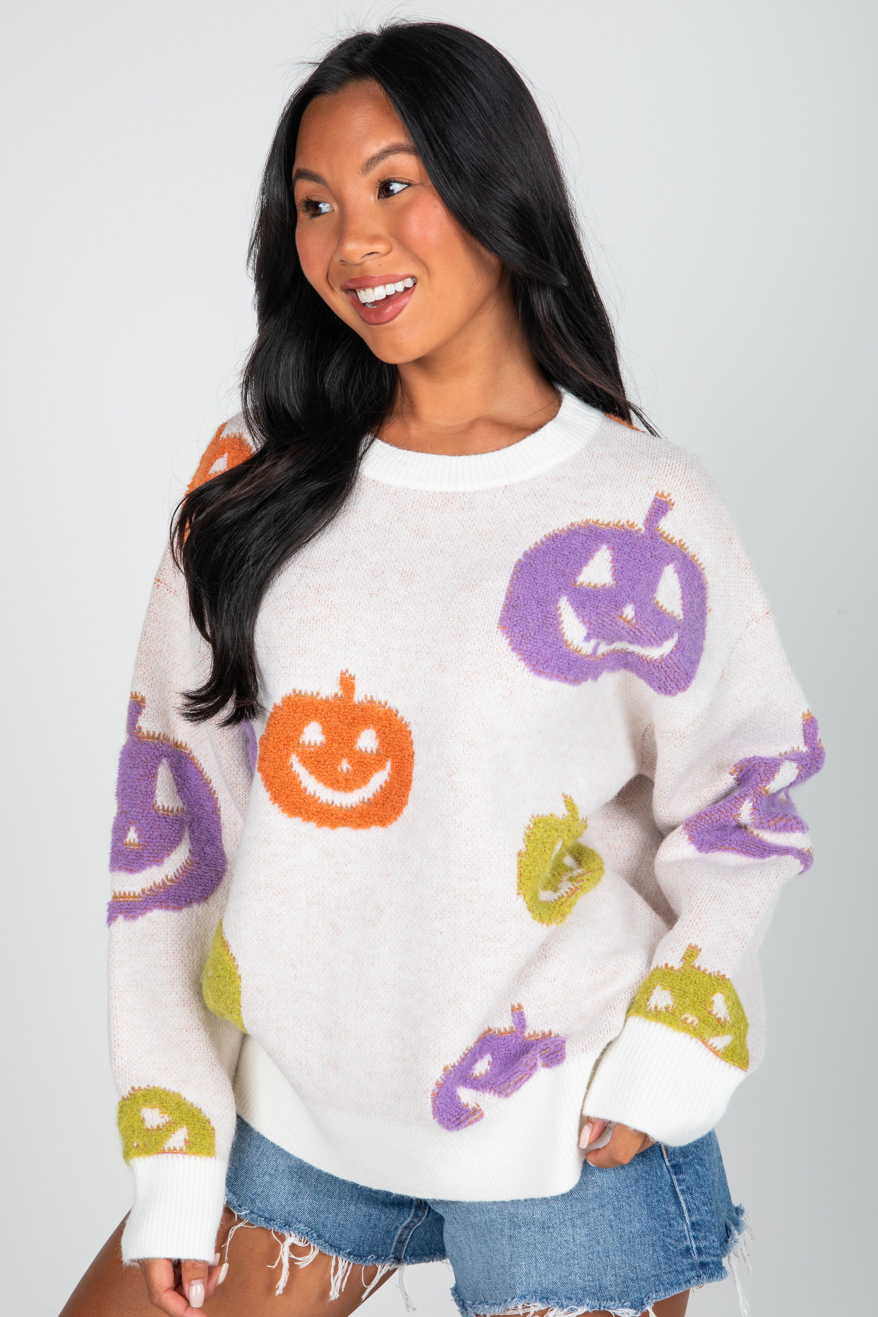Woman wearing a white sweater with colorful pumpkin designs on a plain background