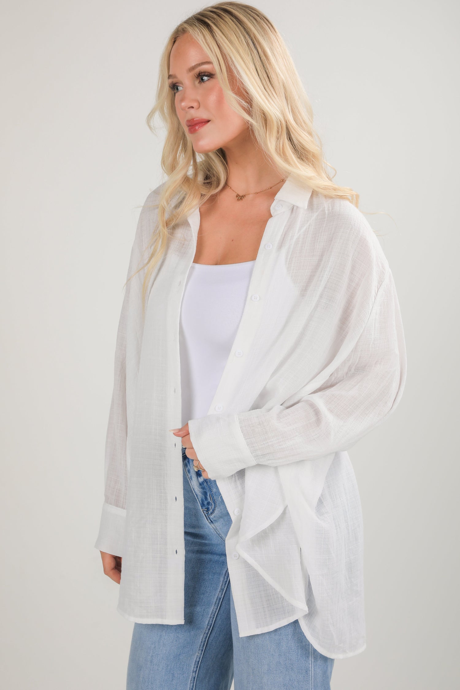 Woman wearing a white oversized shirt and blue jeans on a plain background