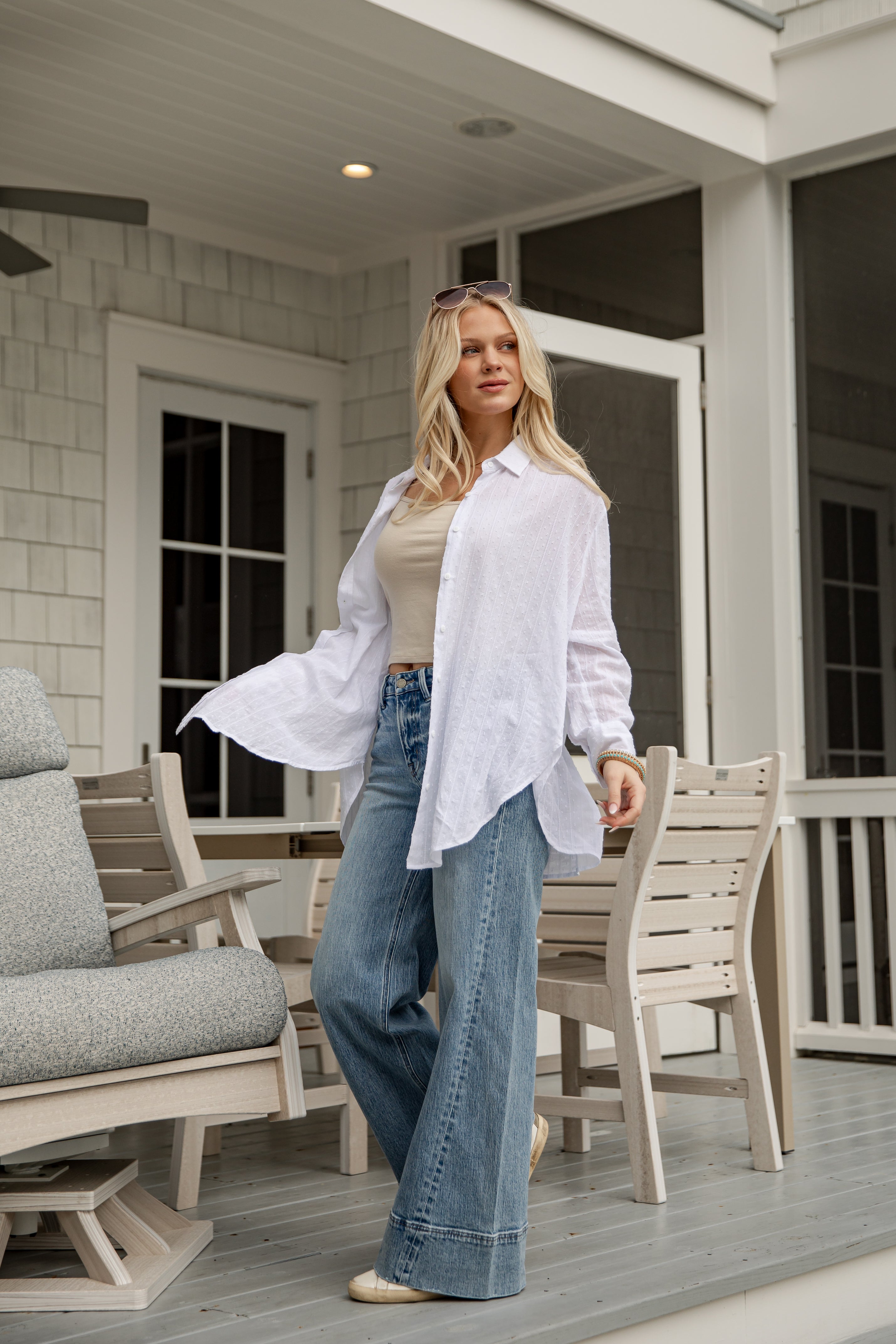 Woman standing on a porch wearing a white shirt and blue jeans.