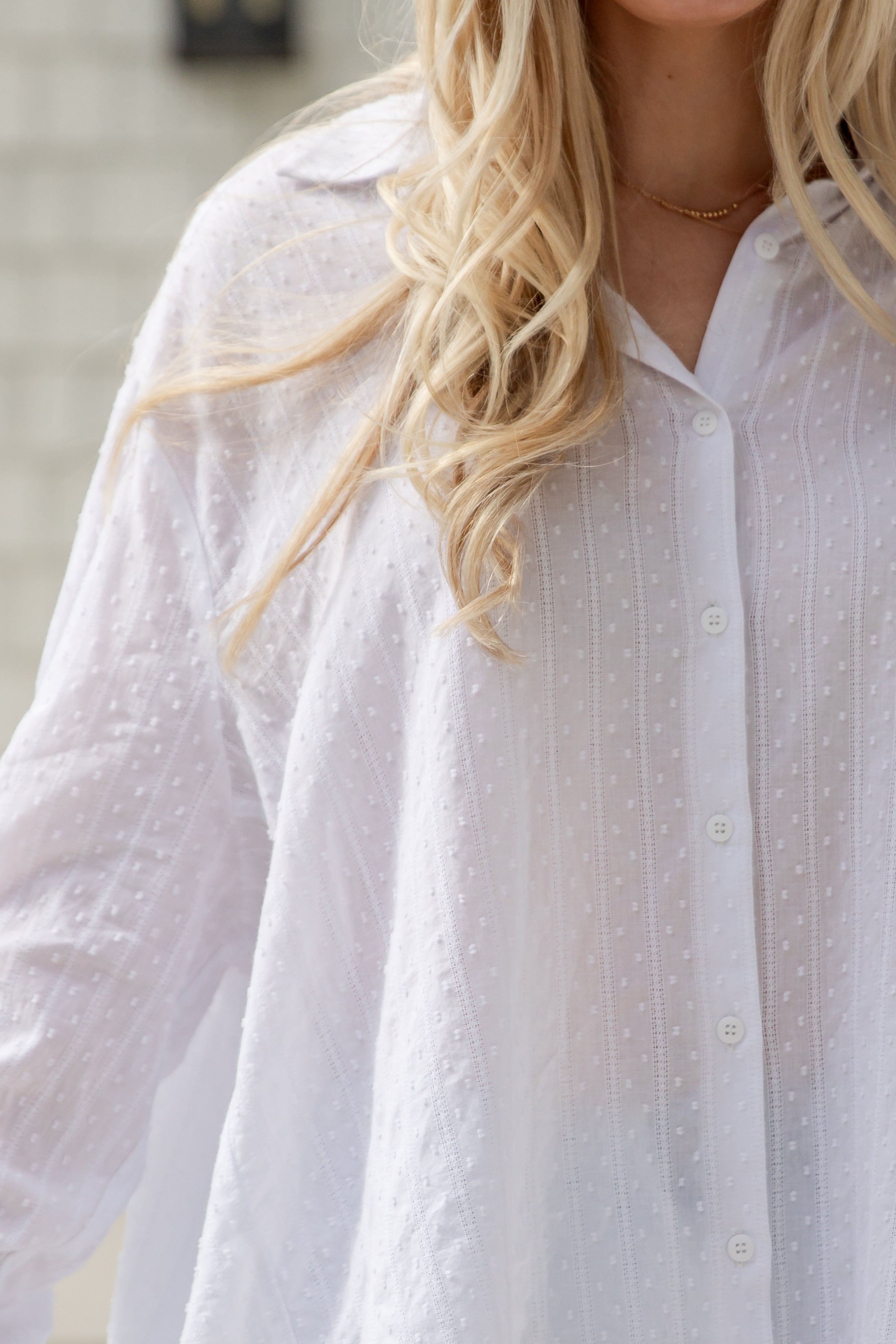 Close-up of a person wearing a white button-up shirt with a blurred background
