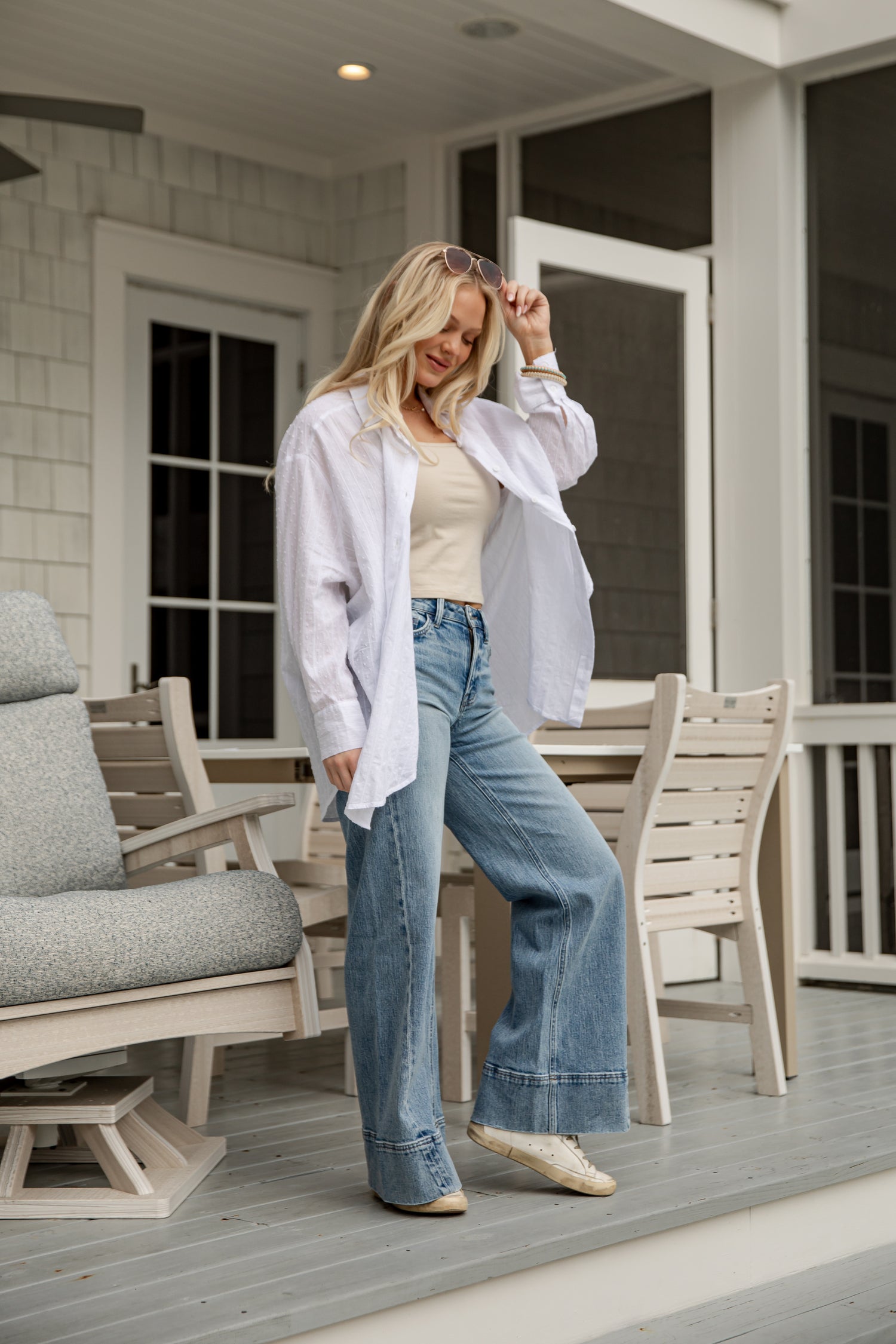 Woman standing on a porch wearing a white shirt and blue jeans.
