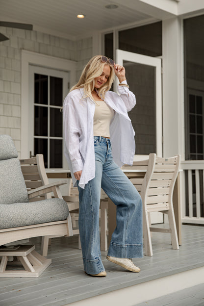 Woman standing on a porch wearing a white shirt and blue jeans.