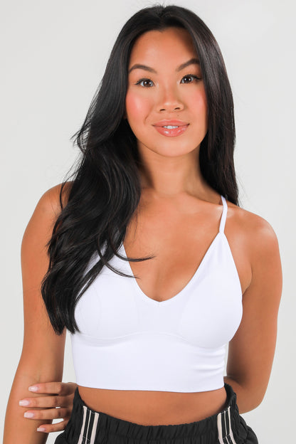 Woman wearing a white sports bra and black athletic pants against a plain background