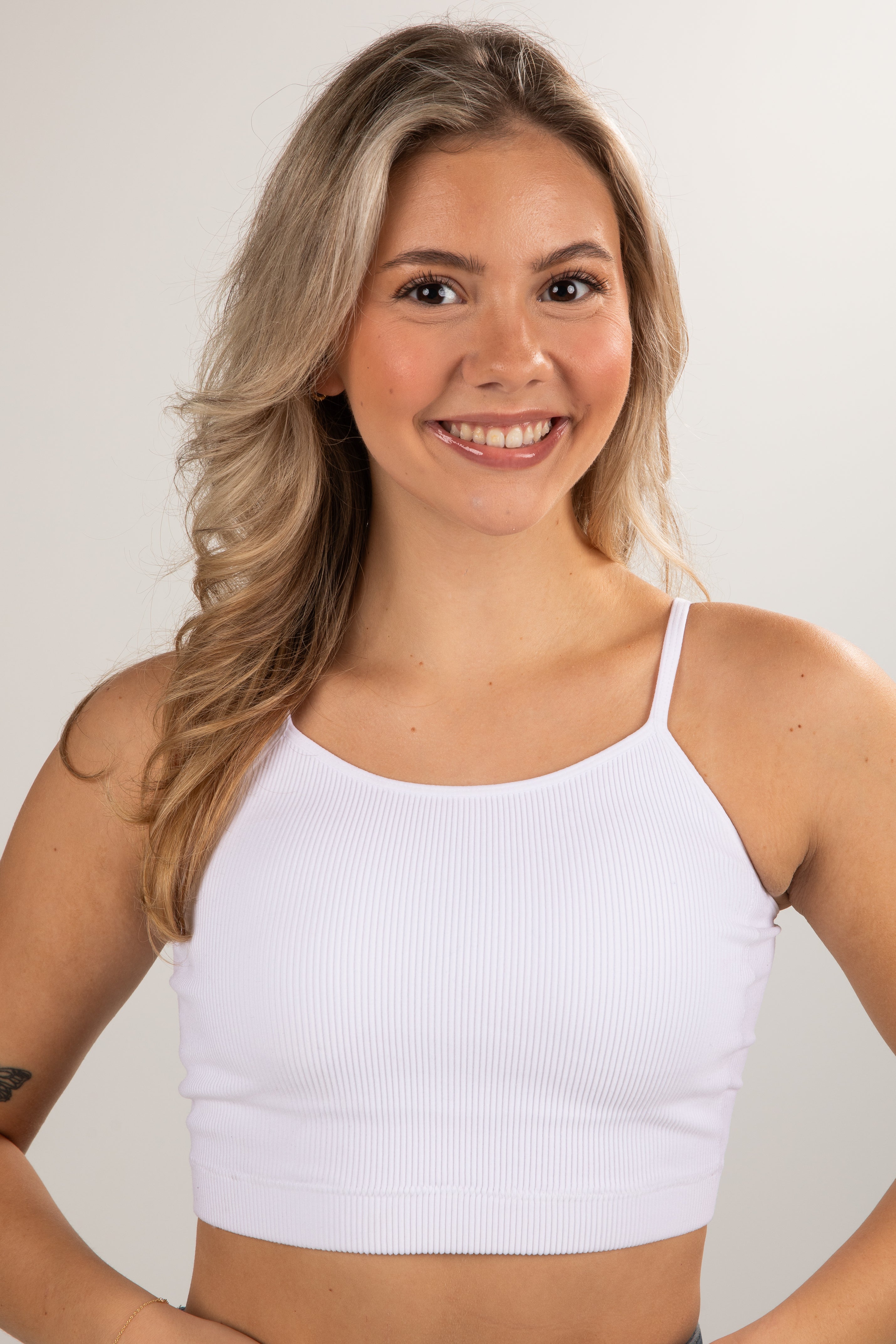 Woman wearing a white tank top against a plain background