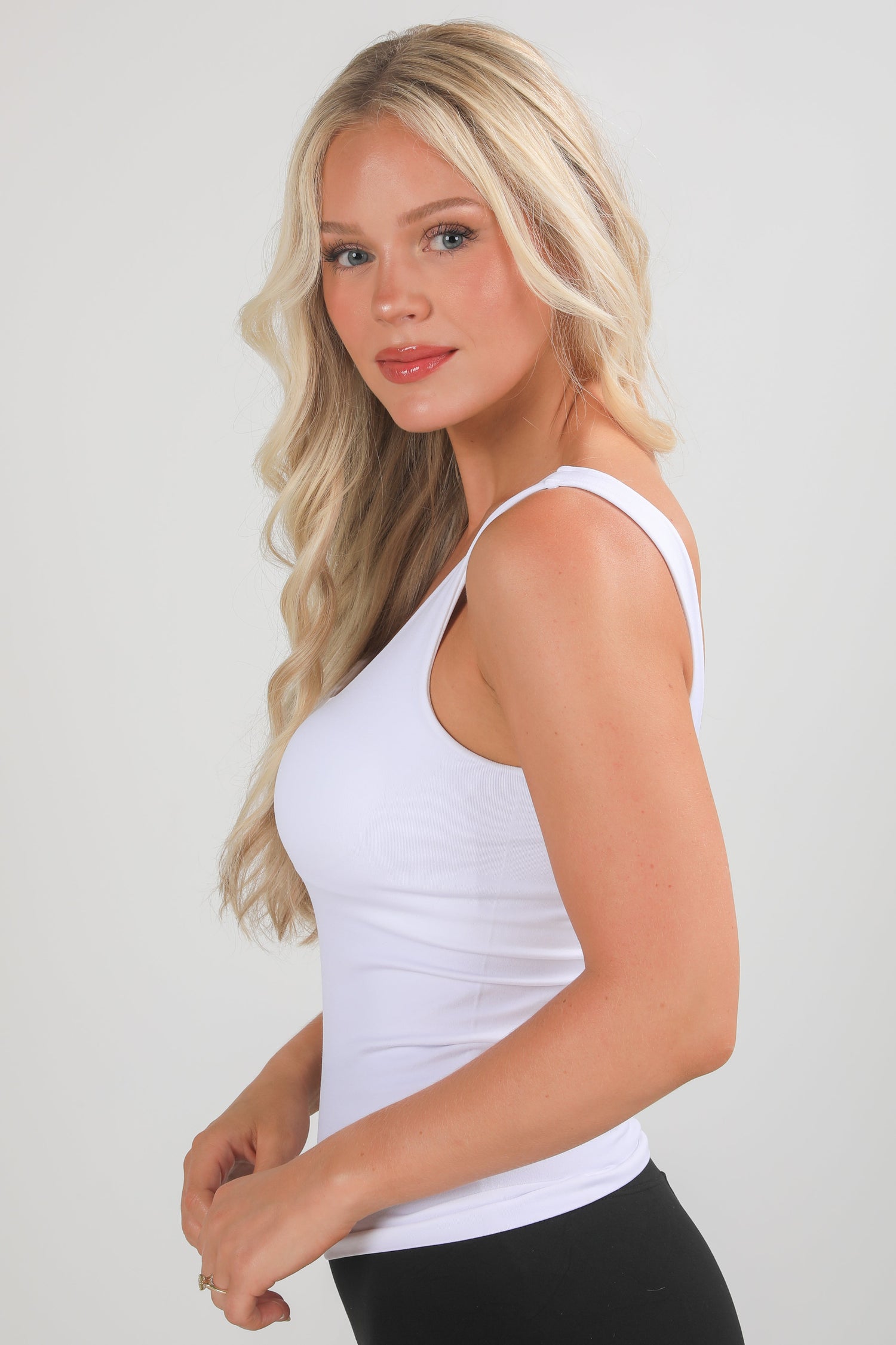 Woman wearing a white tank top against a plain background
